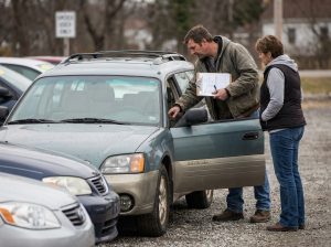 This image shows a buyer inspecting a high-mileage used car, supporting a guide about mileage, service records, engine condition, transmission, repair costs, and pre-purchase inspection.